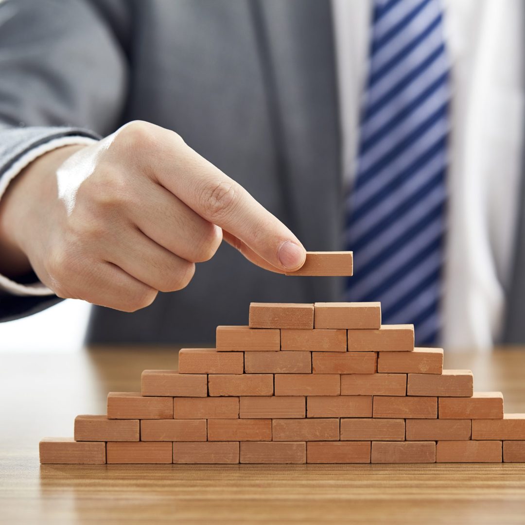 A businessman in a suit putting the last piece of a pyramid using wooden blocks - success concept